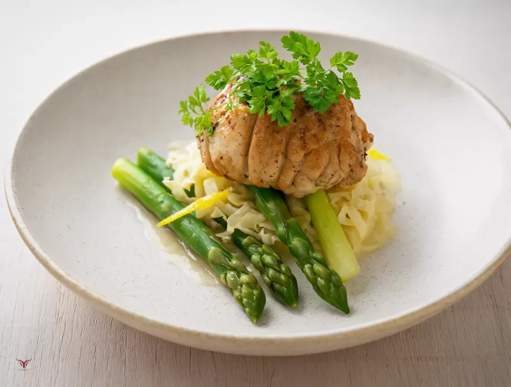 Ris de veau doré servi sur lit d'asperges vertes avec sauce crémeuse et garniture de persil frais sur assiette blanche moderne