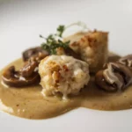 Ris de veau poêlé accompagné de champignons de Paris dans une sauce crémeuse onctueuse, garni d'herbes fraîches, plat gastronomique raffiné