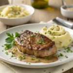 Assiette de foie de veau poêlé doré et fondant, garnie de persil, avec une purée de pommes de terre et une sauce légère, sur une table en bois.