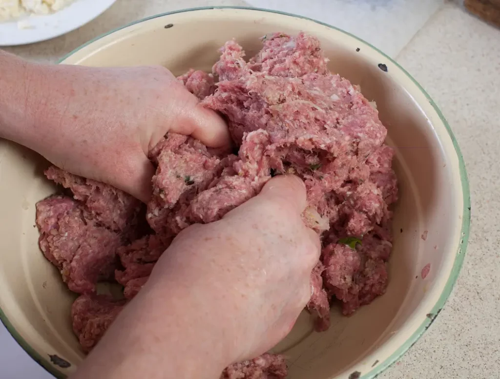 Deux mains mélangent de la viande hachée dans un bol pour former des boulettes.