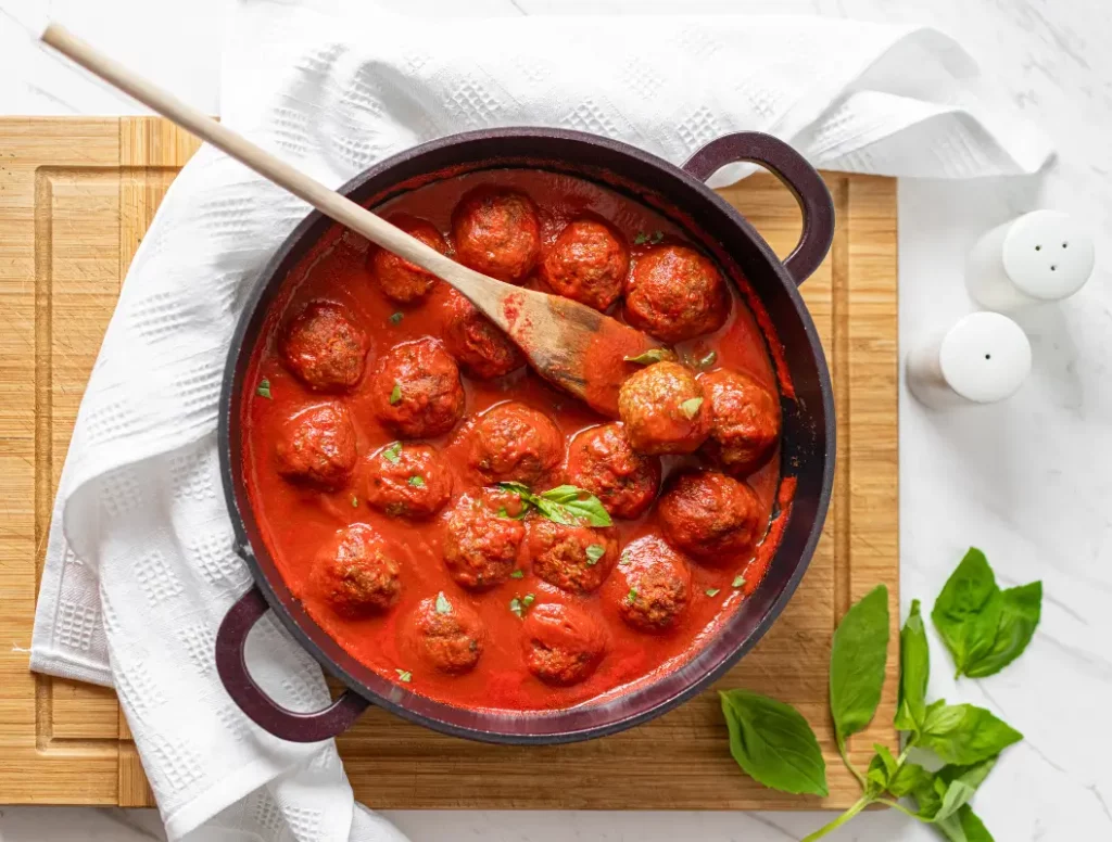 boulettes de viande dans une sauce tomate dans une poêle, avec une cuillère en bois.
