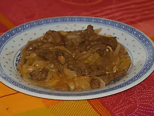 Bœuf aux oignons à la chinoise dans un plat en céramique, nappé de sauce brune.