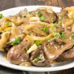 Plat de foie de veau à la lyonnaise traditionnel, servi dans un bol rustique, avec des oignons confits et une sauce brillante.