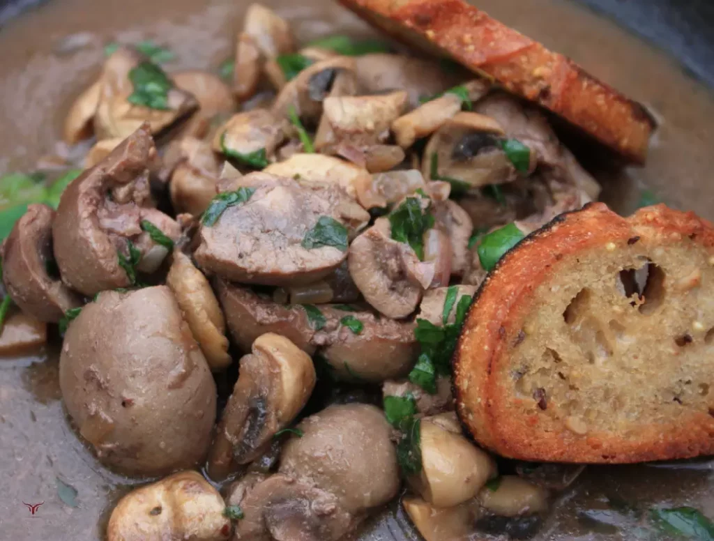 Plat de rognons de veau cuisinés à la française avec des champignons et une sauce riche, servi dans une assiette creuse.
