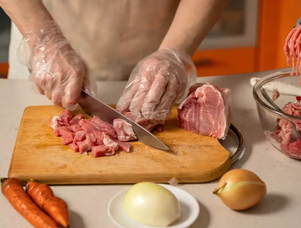 Les mains du créateur du blog Recettes Carnées préparant une pièce de viande avec des herbes et de l'ail sur une planche en bois, pour la page à propos.