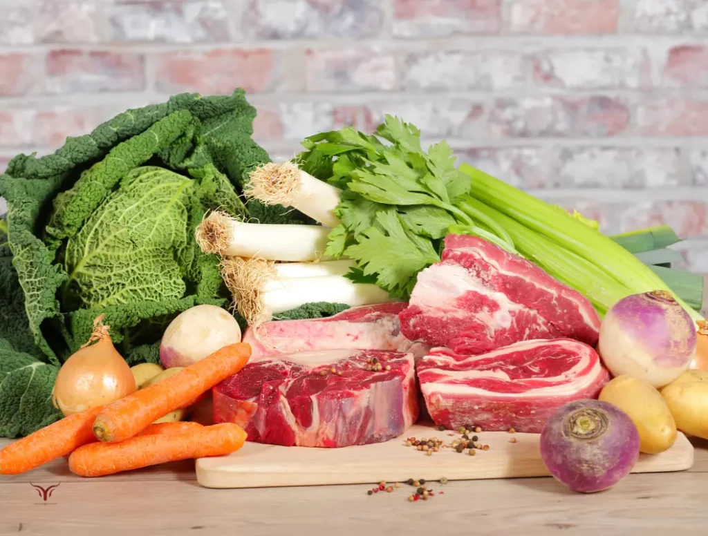 Sélection complète d'ingrédients pour pot-au-feu traditionnel : variété de viandes de bœuf (jarret, plat de côtes), légumes frais (carottes, navets, poireaux, céleri, chou, pommes de terre, oignons) et épices sur planche bois